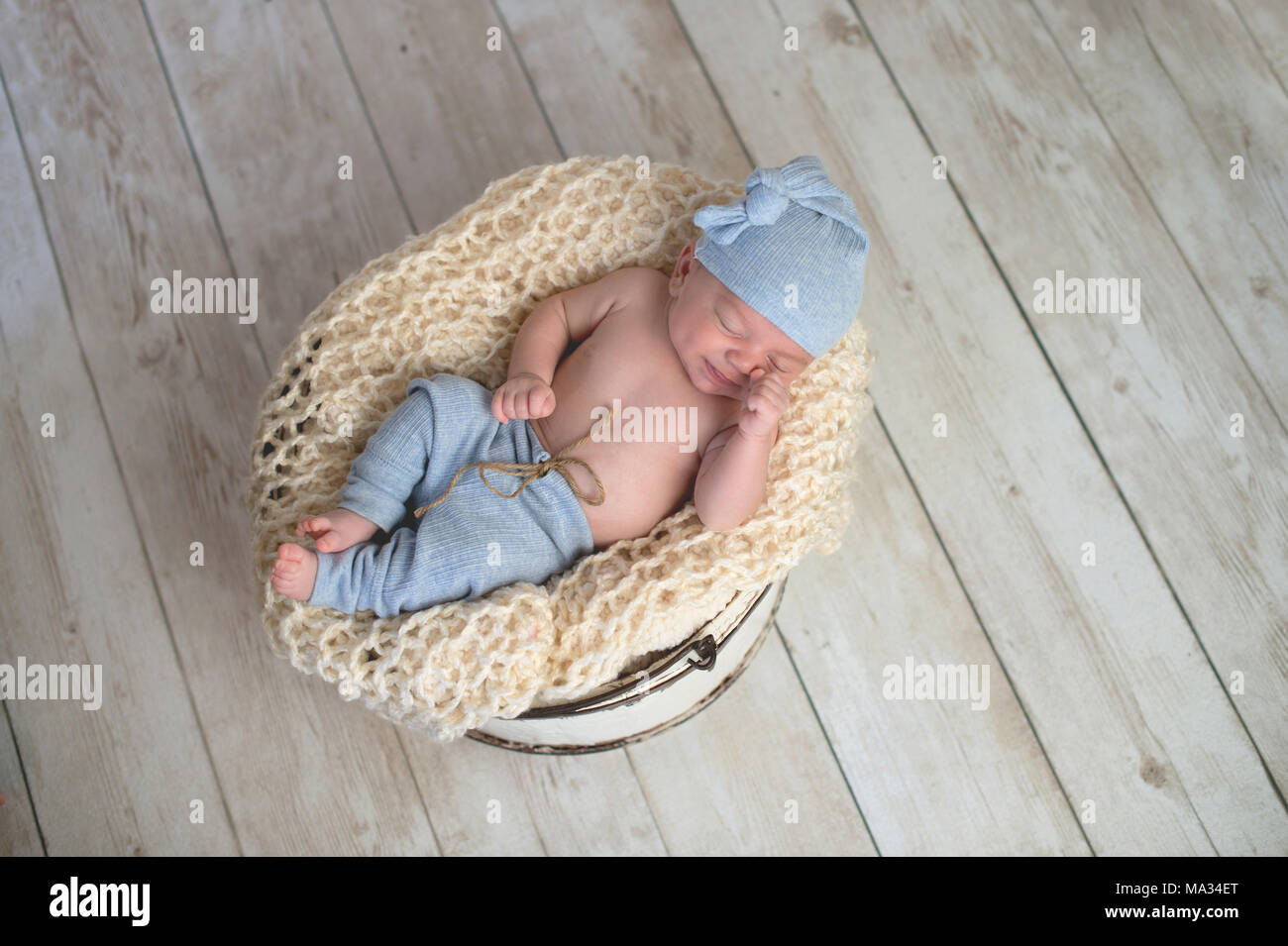 Six week old baby boy wearing light blue pjs and lying in a round, bucket. Shot in the studio on a light wood background. Stock Photo