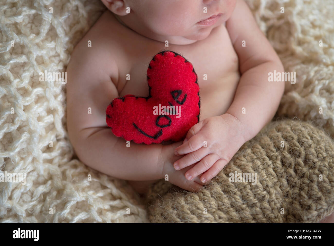 Six week old baby holding a heart shaped pillow with the word love