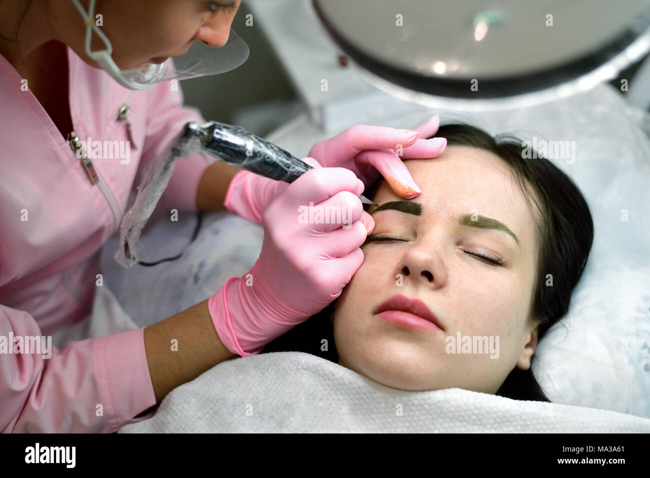 the master does the tattoo on the eyebrows to the girl. Stock Photo