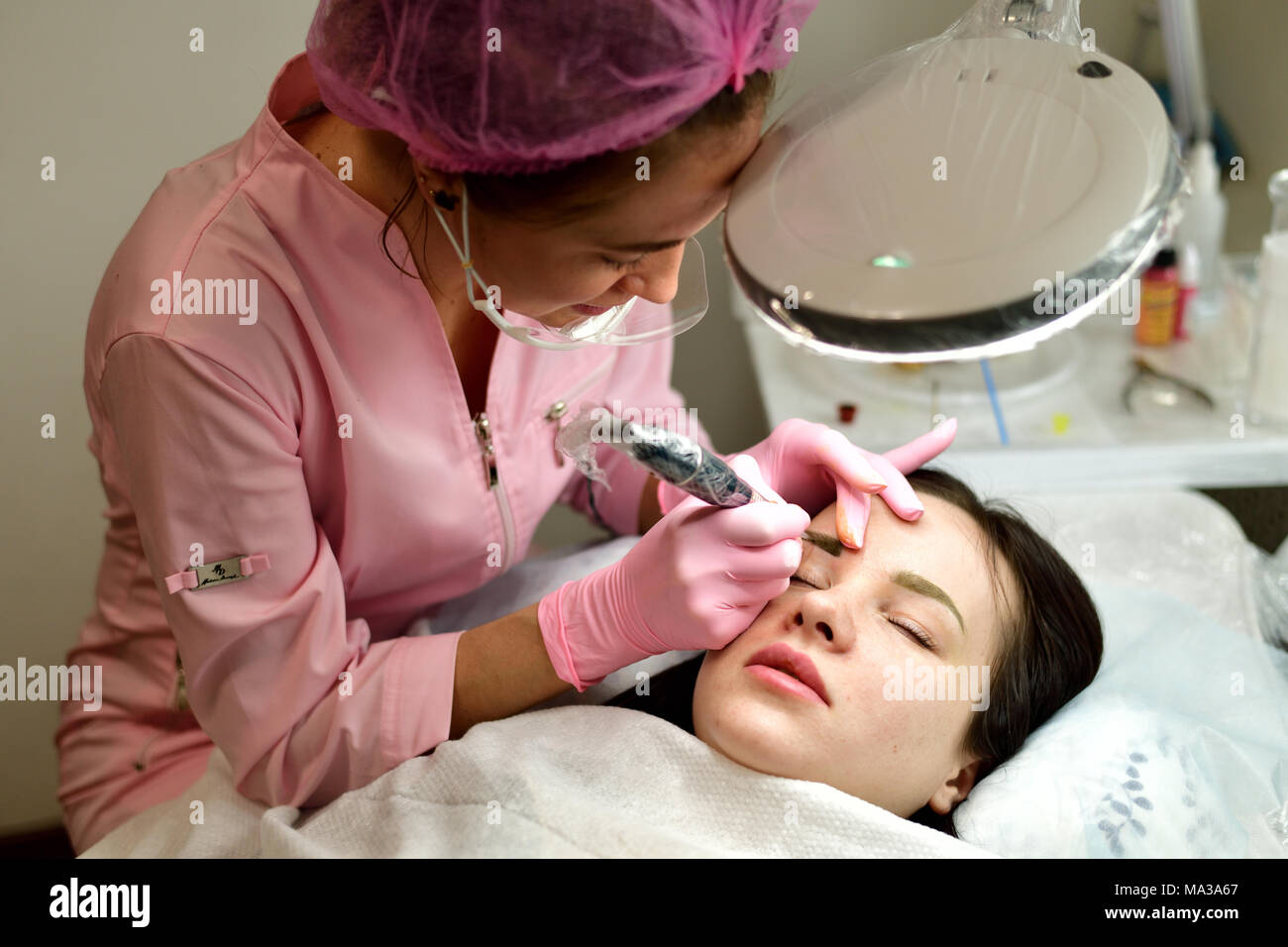 the master does the tattoo on the eyebrows to the girl. Stock Photo