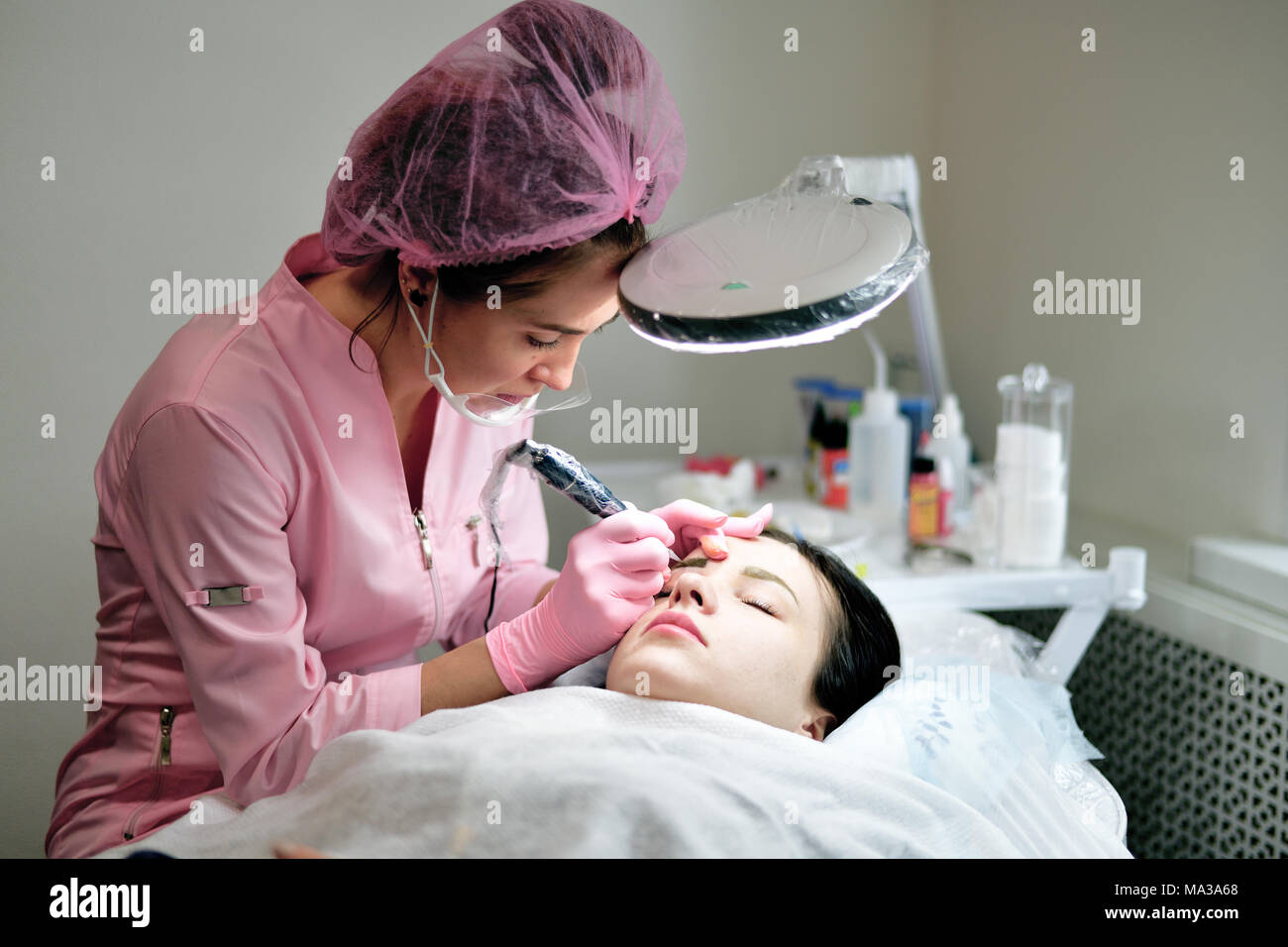 the master does the tattoo on the eyebrows to the girl. Stock Photo