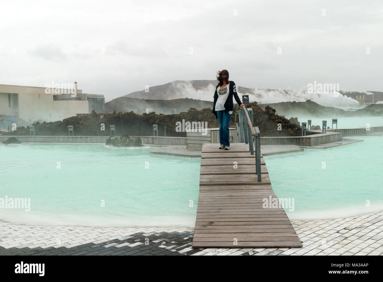 Woman standing windblown on a bridge at the Blue Lagoon open air geothermal swimming pool and spa, Iceland. Stock Photo