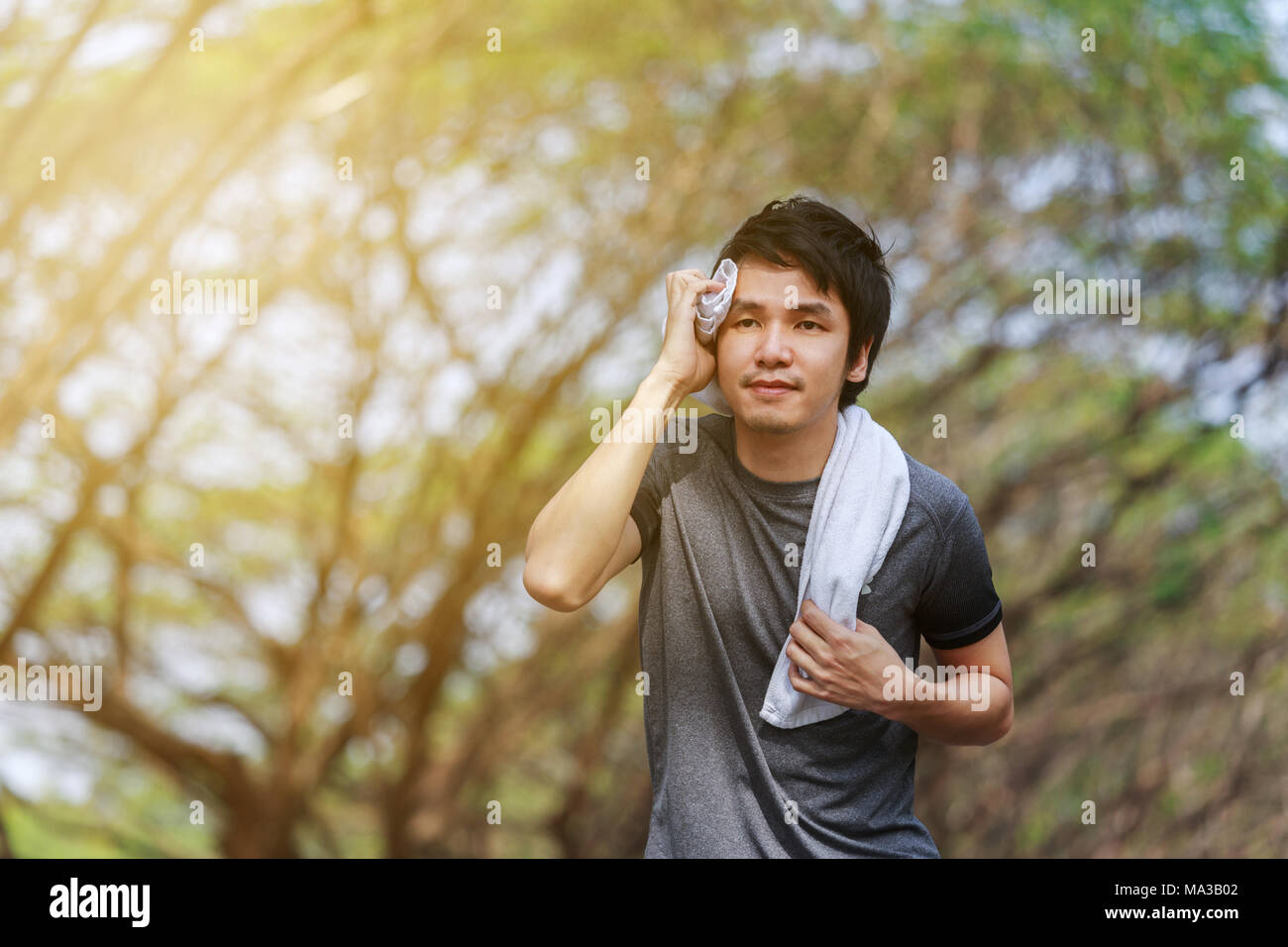 young sporty man running and wiping his sweat with a towel in the park Stock Photo