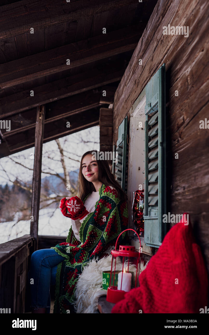 young woman,wrapped in a blanket sitting on the balcony and holding a ...