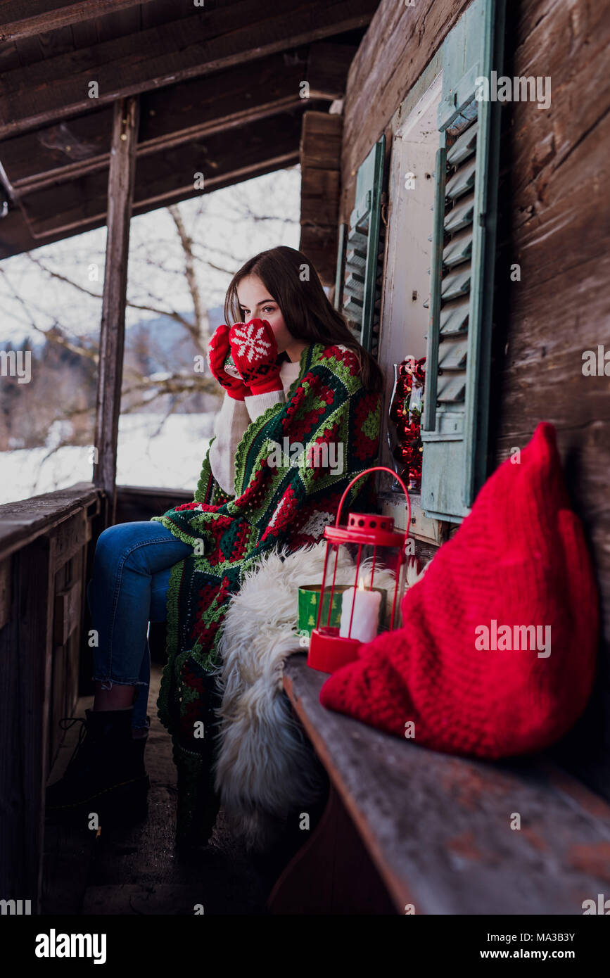 young woman,wrapped in a blanket sitting on the balcony and holding a ...
