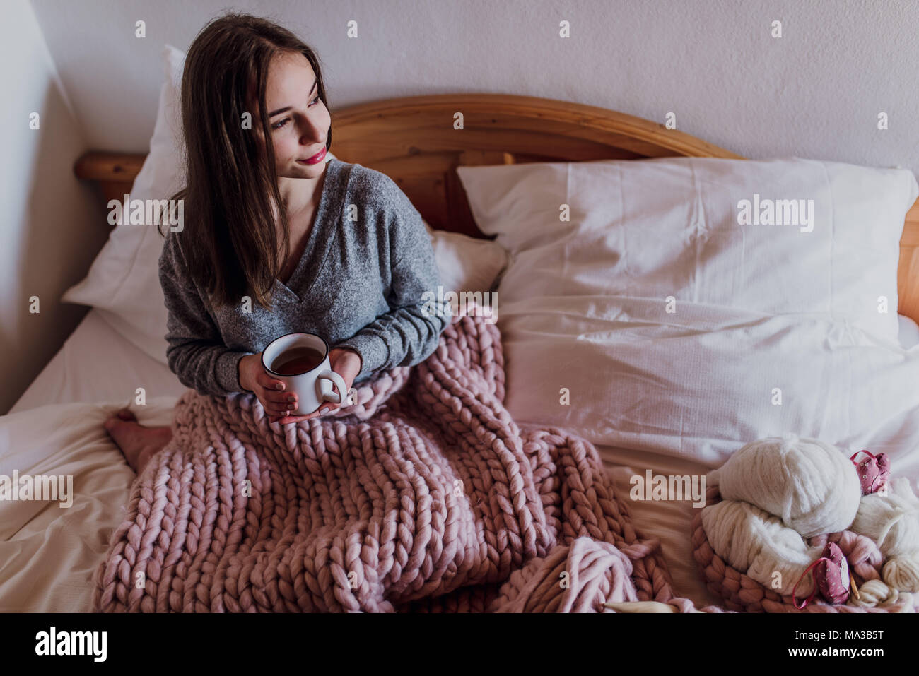 young woman sitting in bed with a cup of tea Stock Photo