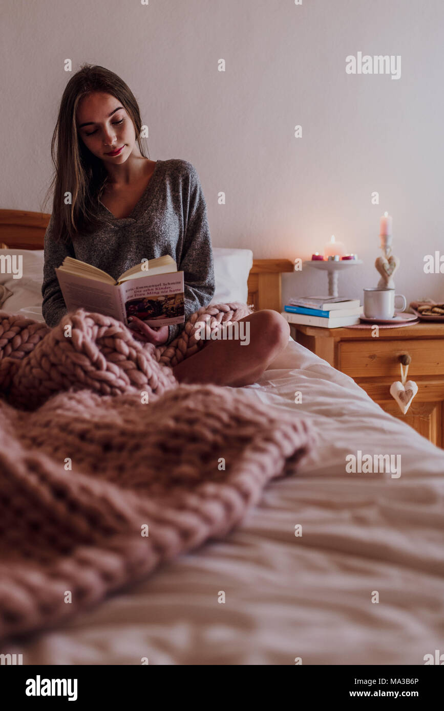 young woman sitting in bed and reading a book Stock Photo