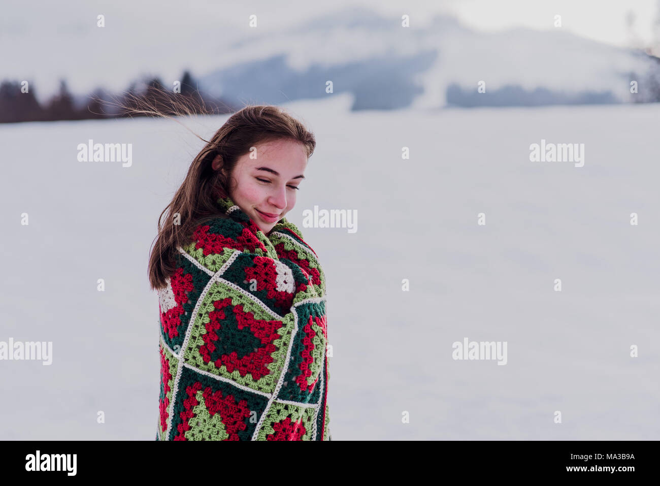 young woman wrapped in a blanket is standing in the snow, Stock Photo