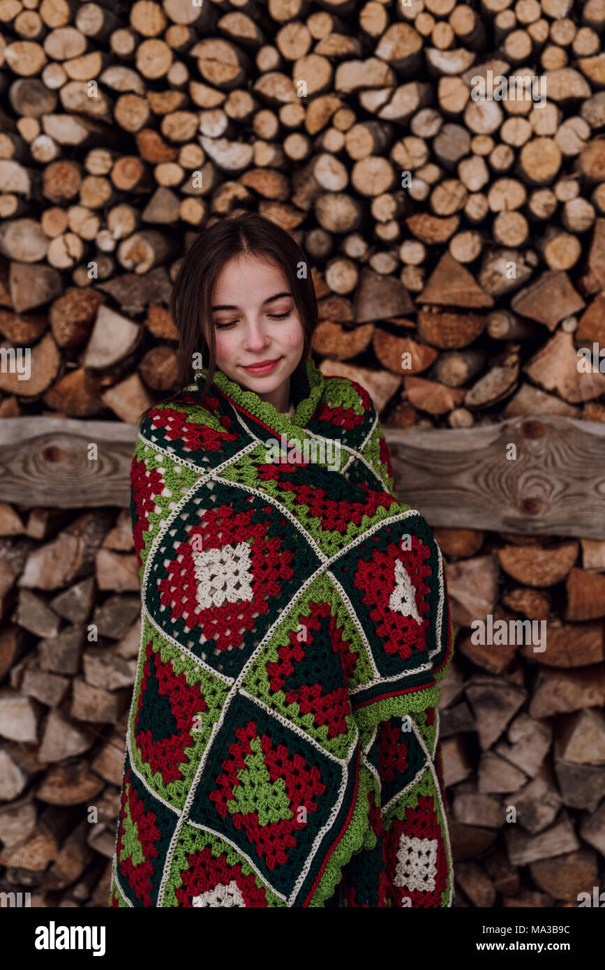 young woman wrapped in a blanket in front of a woodpile Stock Photo