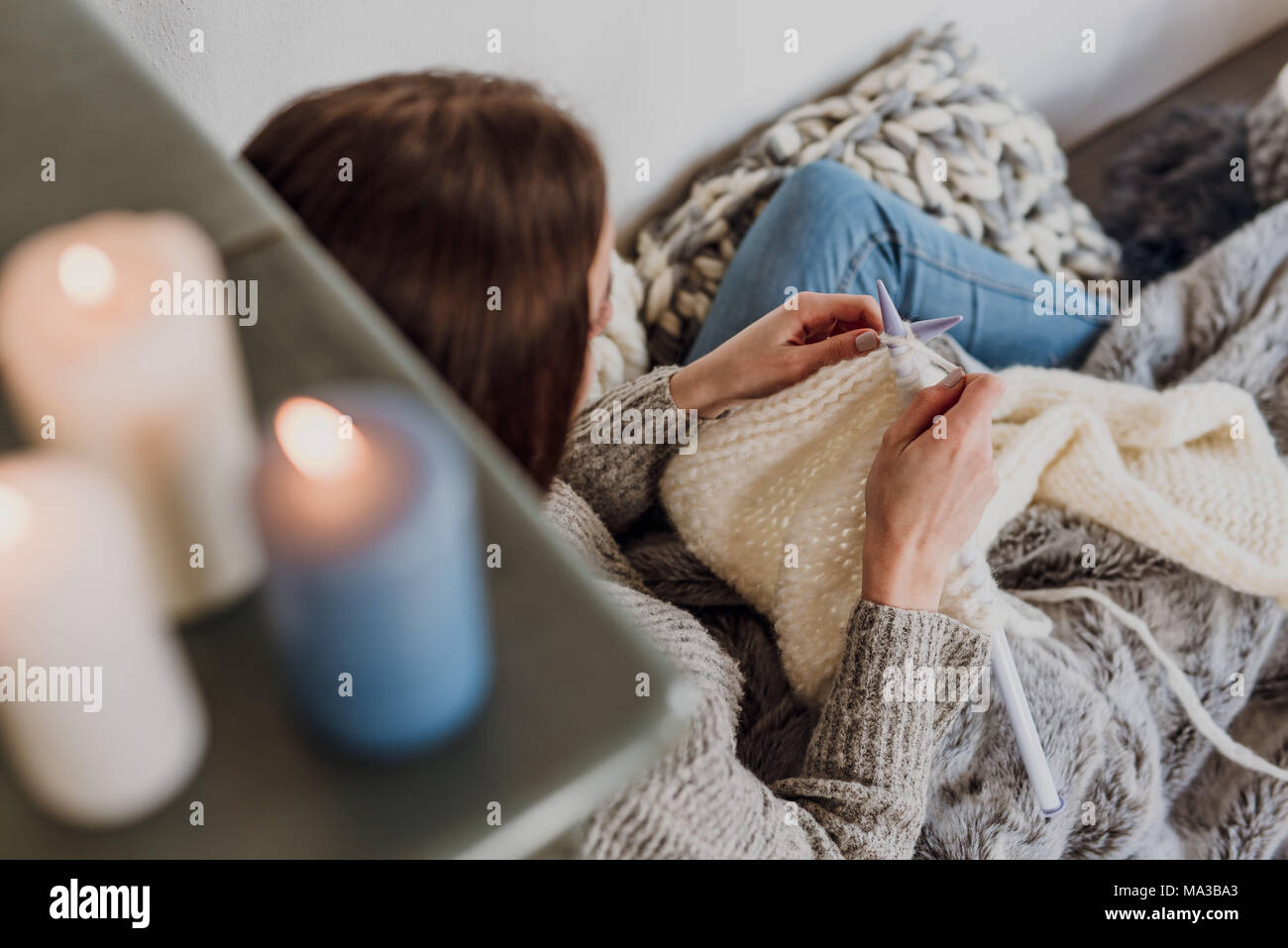 young woman sits next to a tiled stove and knits,detail,candles,blur, Stock Photo