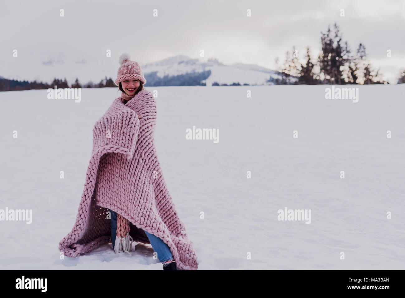 young woman stands wrapped in a pink blanket in wintry landscape, Stock Photo