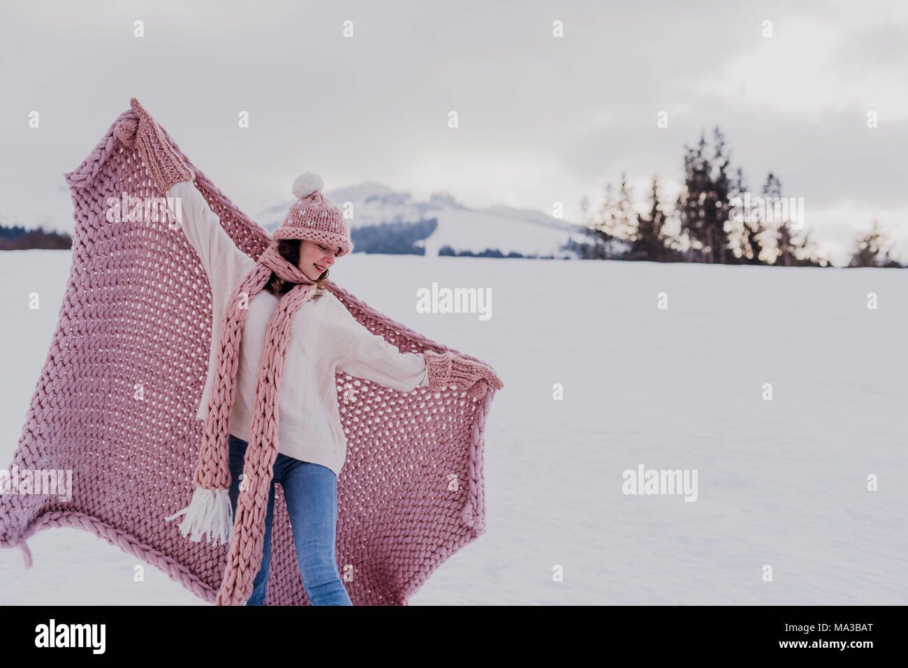 young woman stands with pink blanket,wool cap and scarf in the snow,spread arms, Stock Photo