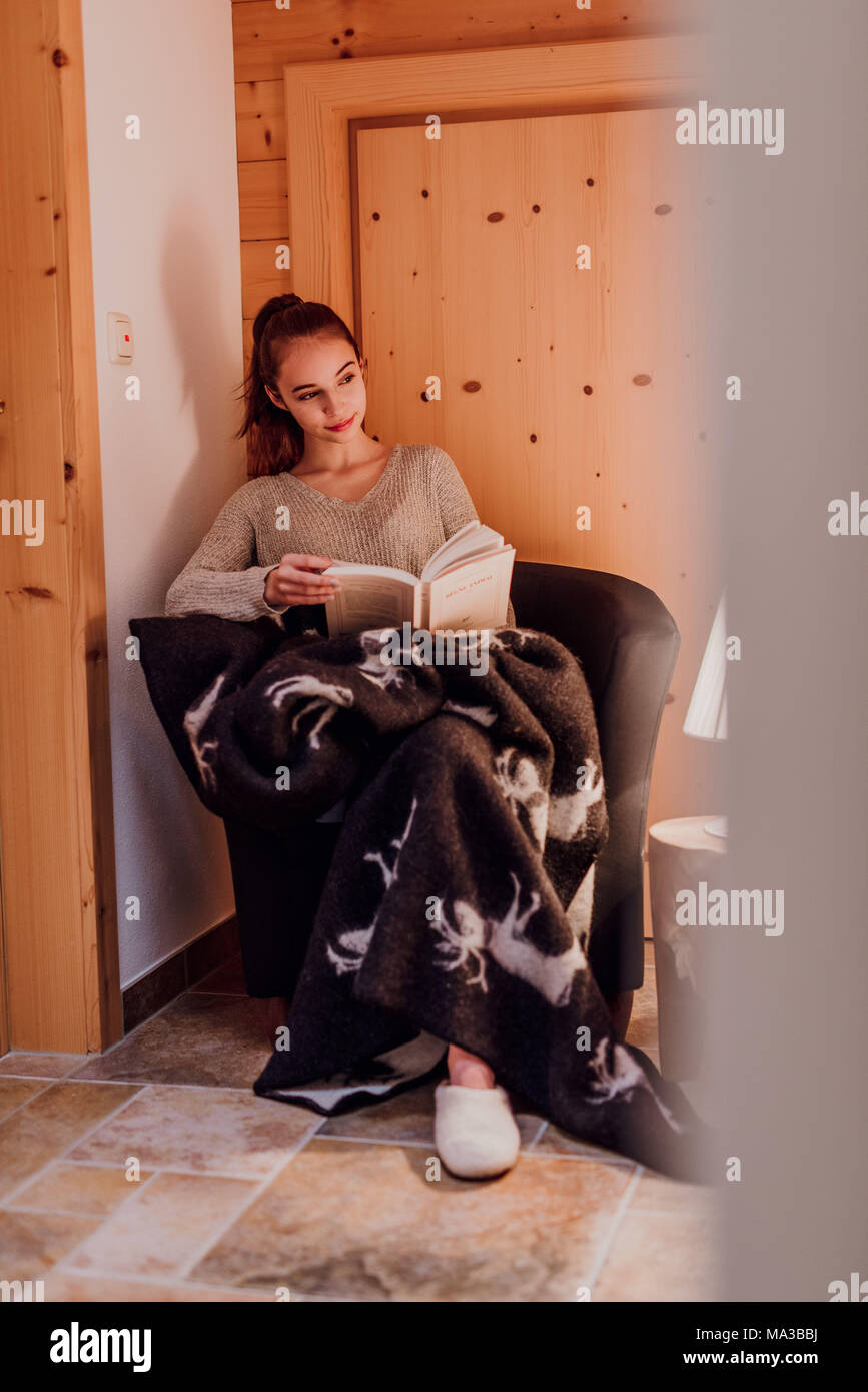 young woman wrapped in a blanket,reading a book,lamp,warm light Stock Photo