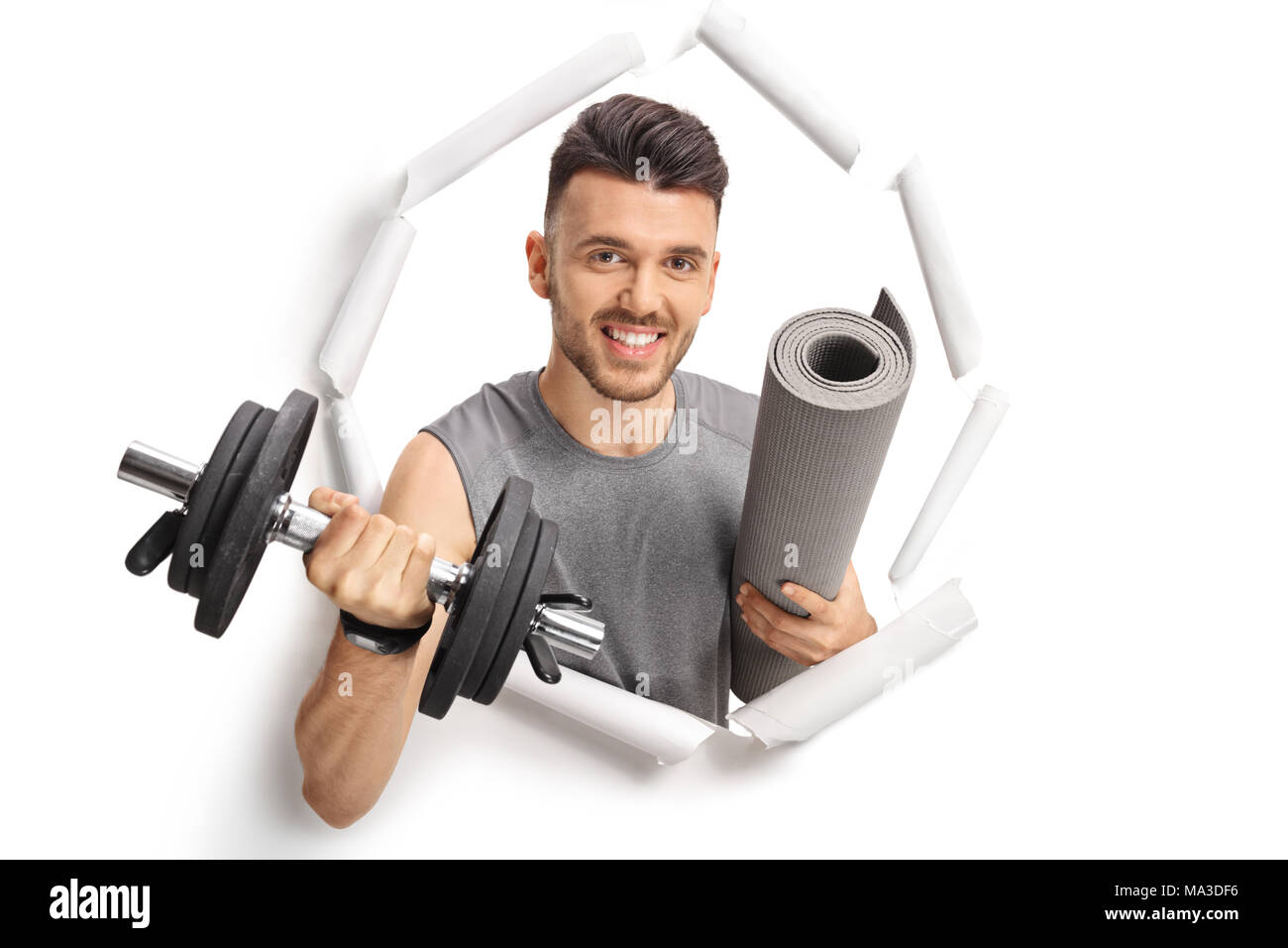 Young man with a dumbbell and an exercise mat breaking through paper Stock Photo