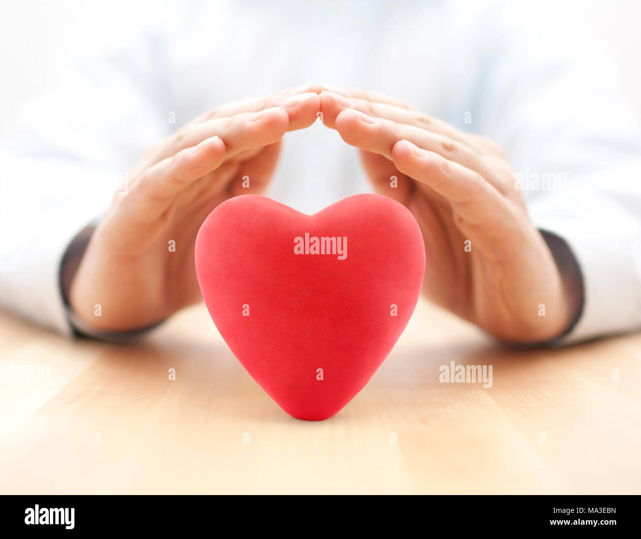 Red heart covered by hands. Health insurance or love concept Stock Photo