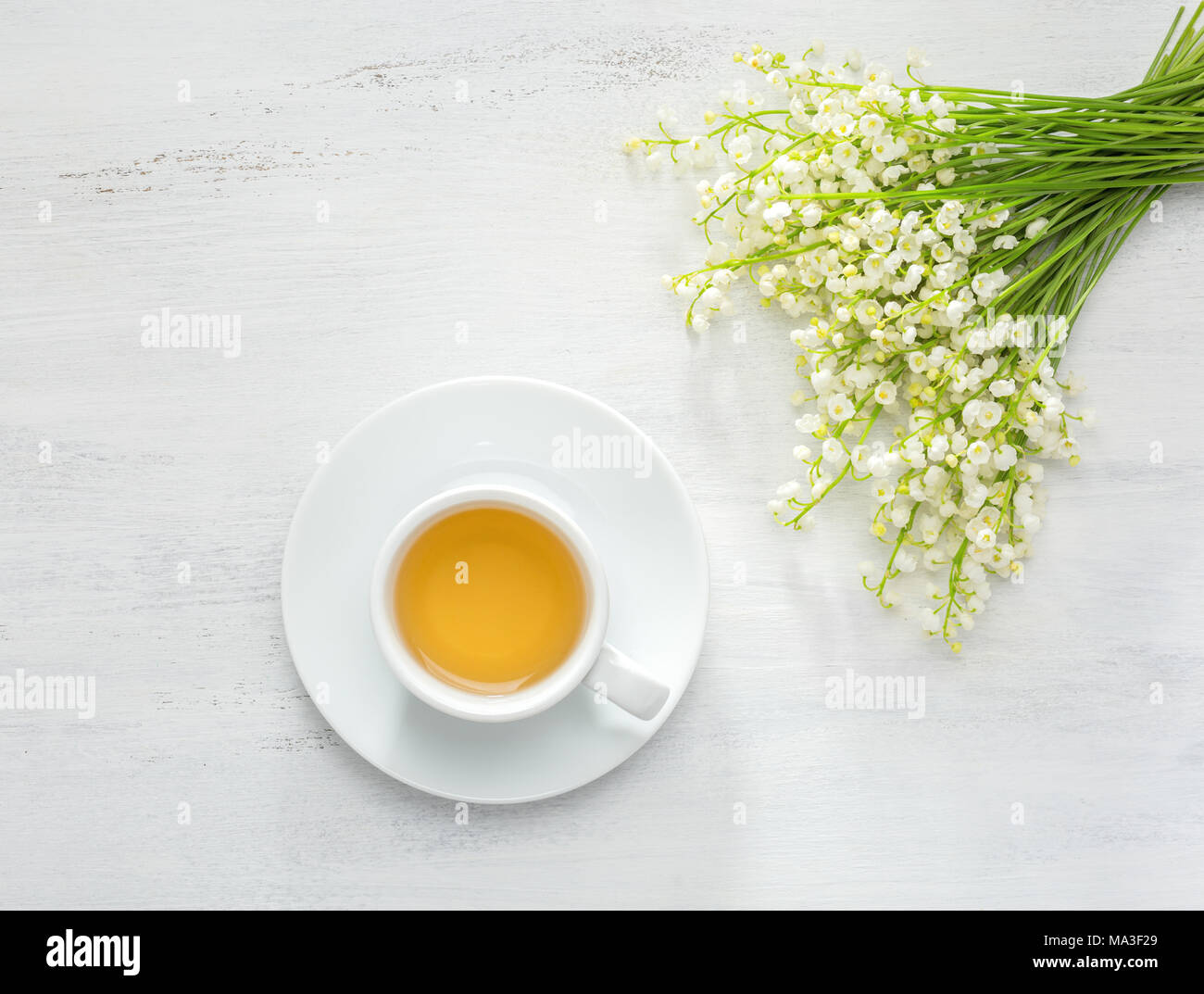 Cup of tea and bouquet of Lilies of the Valley on white rustic table