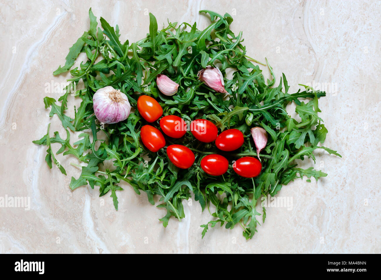 Rocket Arugula with plum tomatoes and garlic for Italian food on marble table Stock Photo