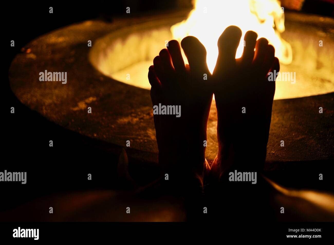 Man resting his bare feet on the cement fire pit ring with flickering
