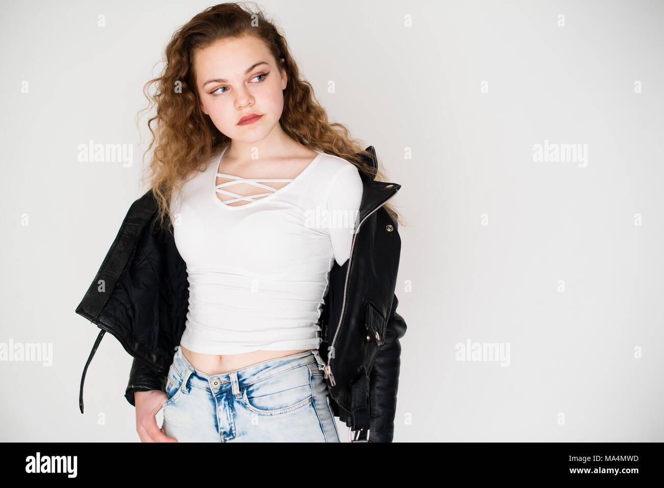A moody attrractive young 13 thirteen year old teenage adolescent girl wearing denim jeans and a black leather jacket , UK Stock Photo