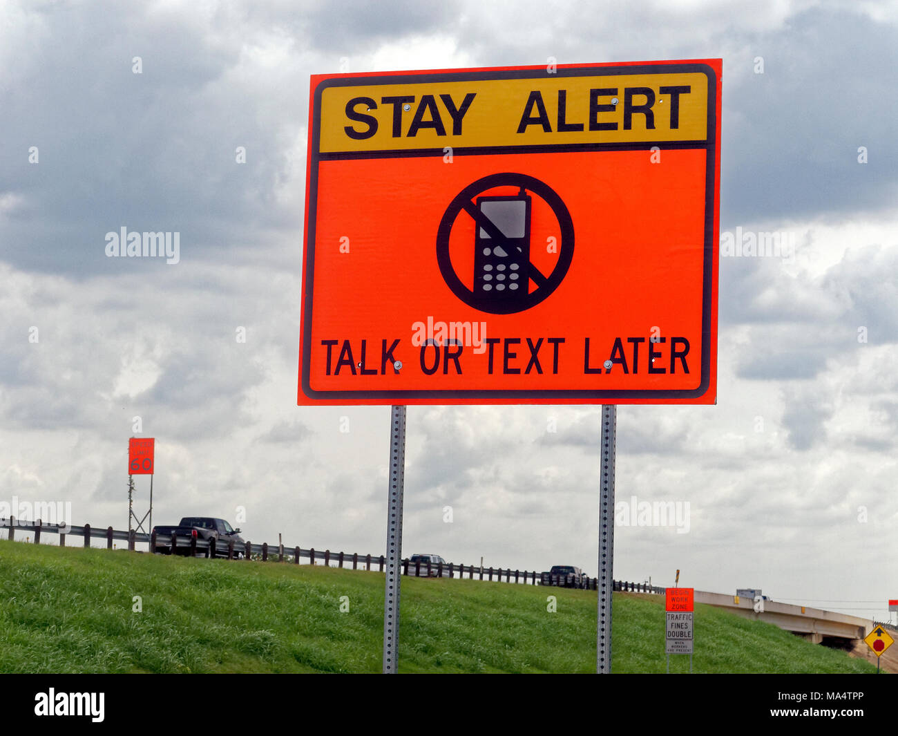 Along the highway a sign warns drivers to stay alert and not to use their smartphone and cellphone while driving. Texting has become a major cause of accidents on today's roads whether on city streets or the motorway. Stock Photo