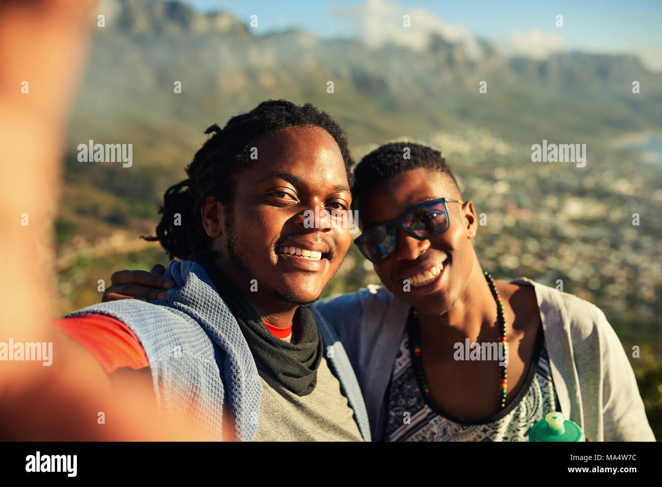 Two happy male african friends take a selfie together while hiking outdoors with gorgeous mountains in the background and true emotion in their smiles Stock Photo
