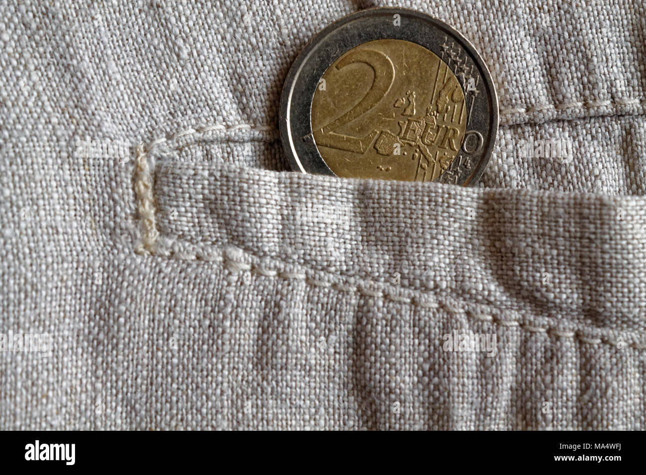 Euro coin with a denomination of two euros in the pocket of worn linen pants Stock Photo