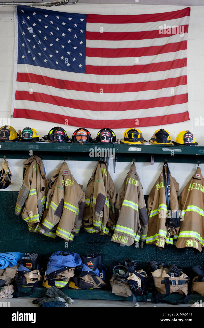 Protective gear, firemen's helmets, and turnout coats along with an American flag on display in the local volunteer firehouse Stock Photo