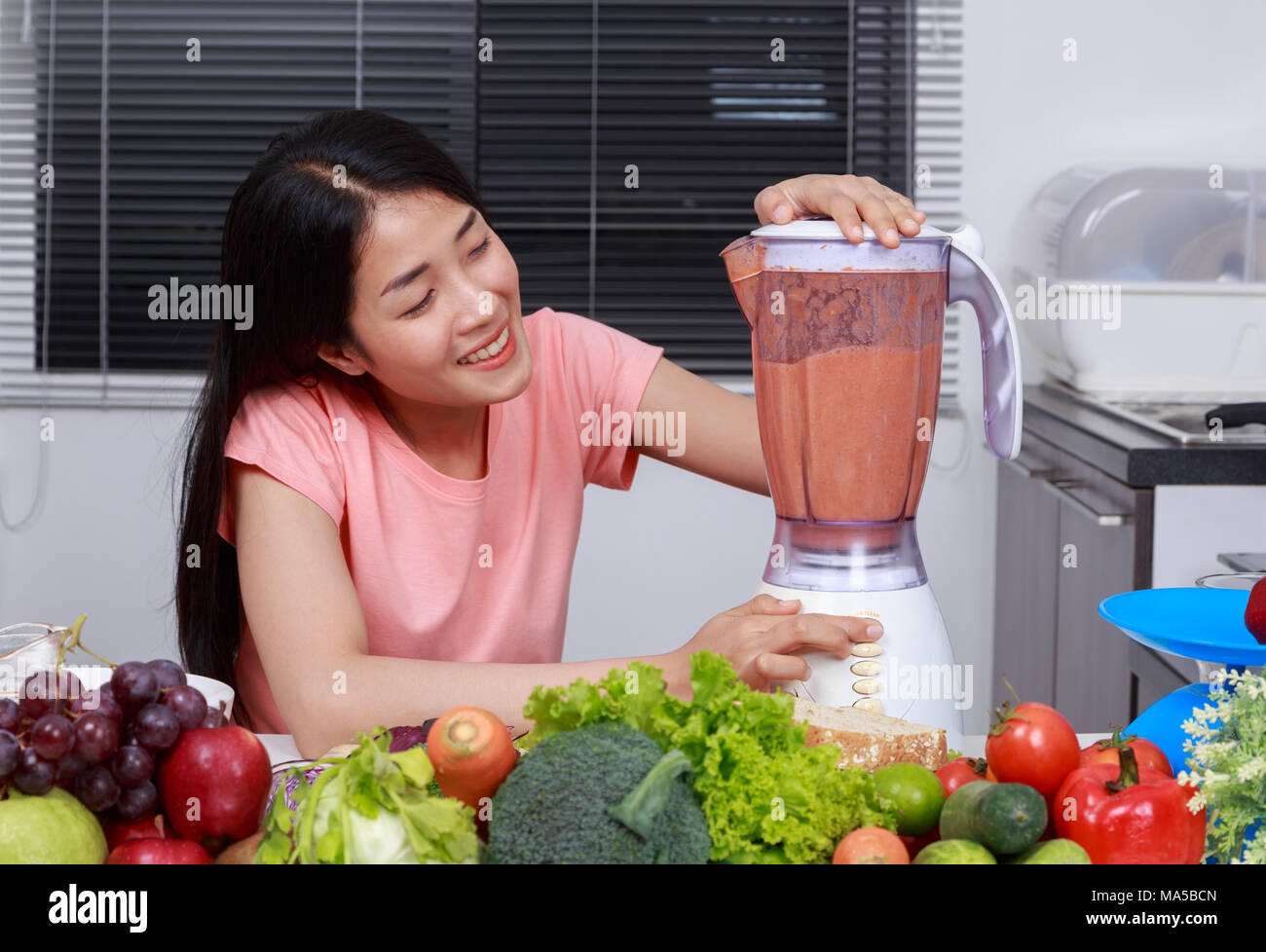 young woman making smoothies with blender in kitchen Stock Photo