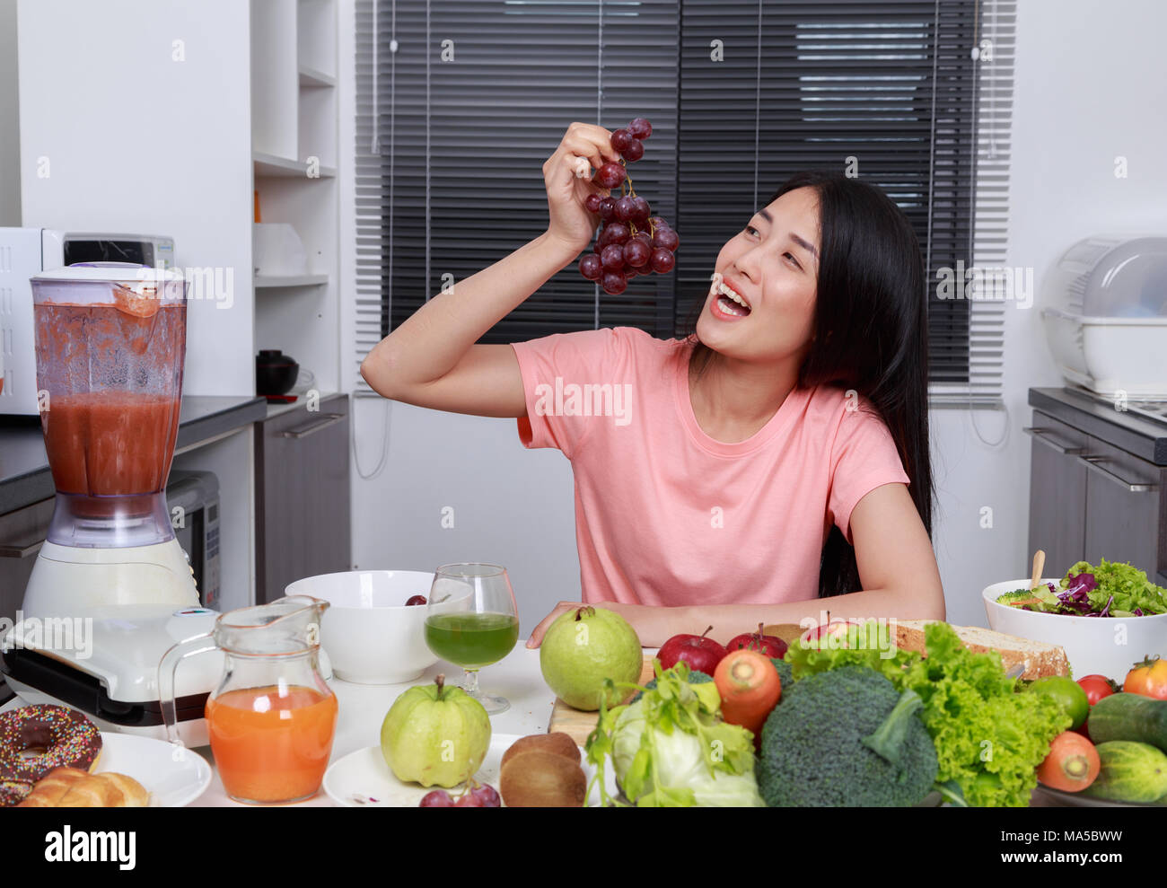 young woman eating grape in kitchen room Stock Photo