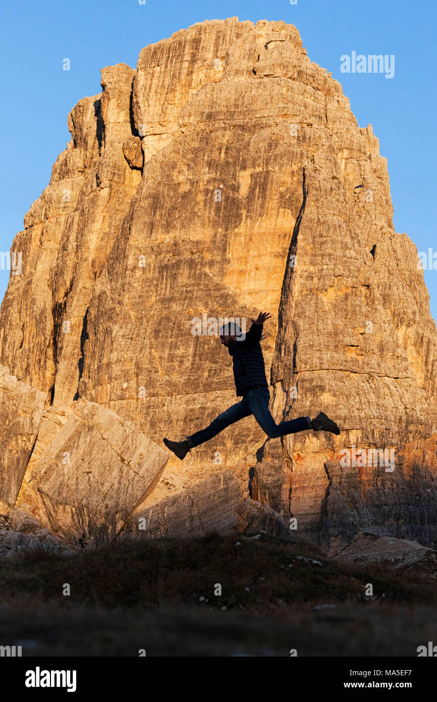 A hiker jumps in fornt of Cinque Torri, Dolomites, Cortina d'Ampezzo, Belluno province, Veneto, Italy Stock Photo