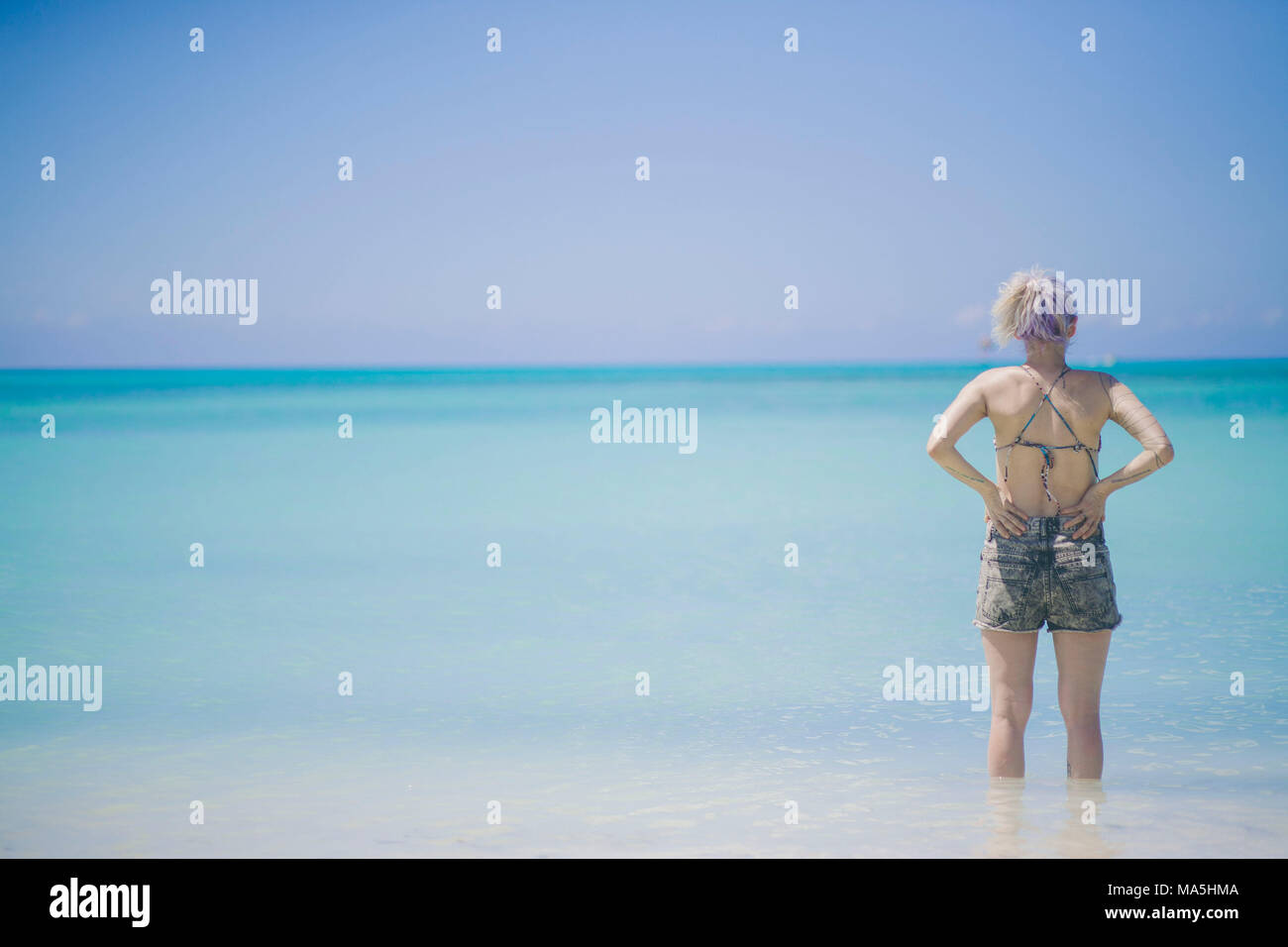 young white hair girl staring to the deep ocean in aruba looking to the turquoise sea Stock Photo