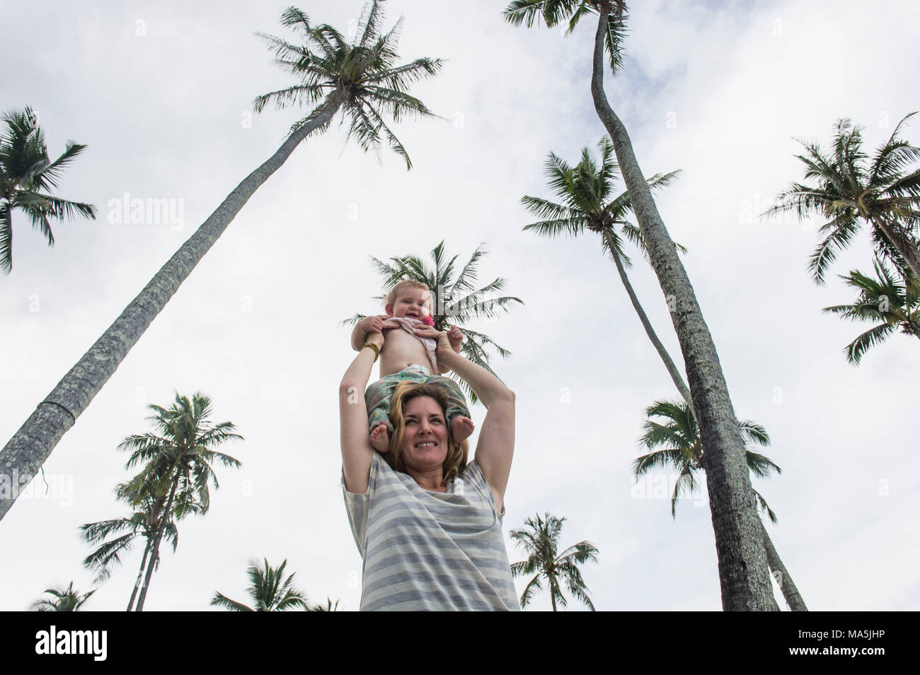 Mother holding her baby undeneath huge palm trees, Temae public beach, Moorea, French Polynesia Stock Photo
