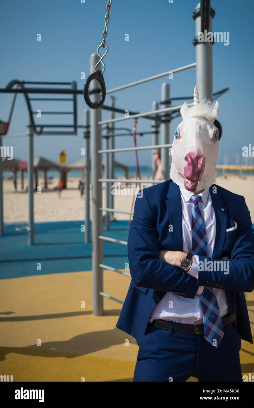 Unusual fitness trainer in suit and mask welcomes you at sport ground near beachfront. Strange man ready to pump the muscles. Unicorn fitness outdoors Stock Photo
