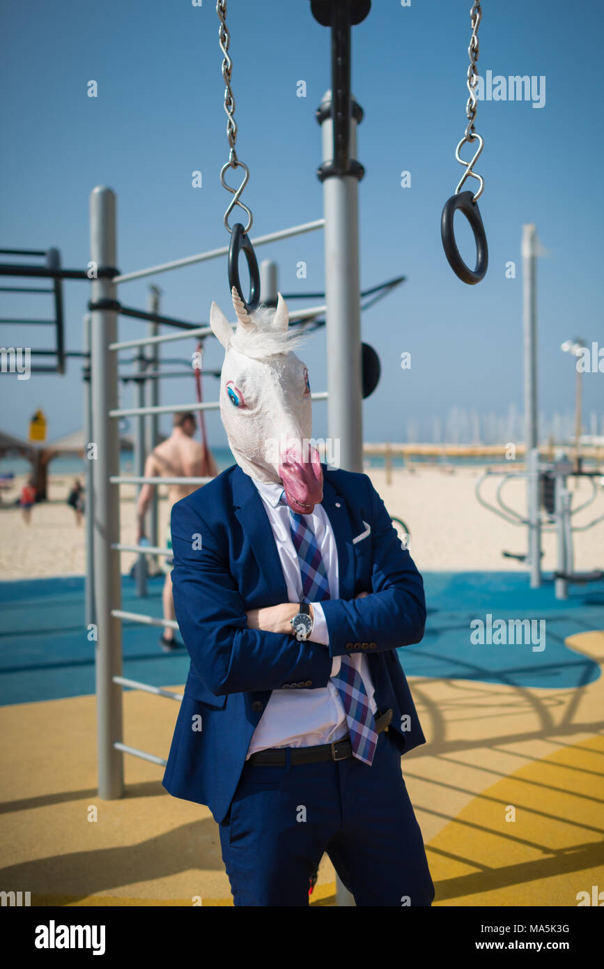 Funny fitness trainer in suit and mask welcomes you at sport ground. Unusual strange man ready to pump the muscles. Unicorn fitness outdoors Stock Photo