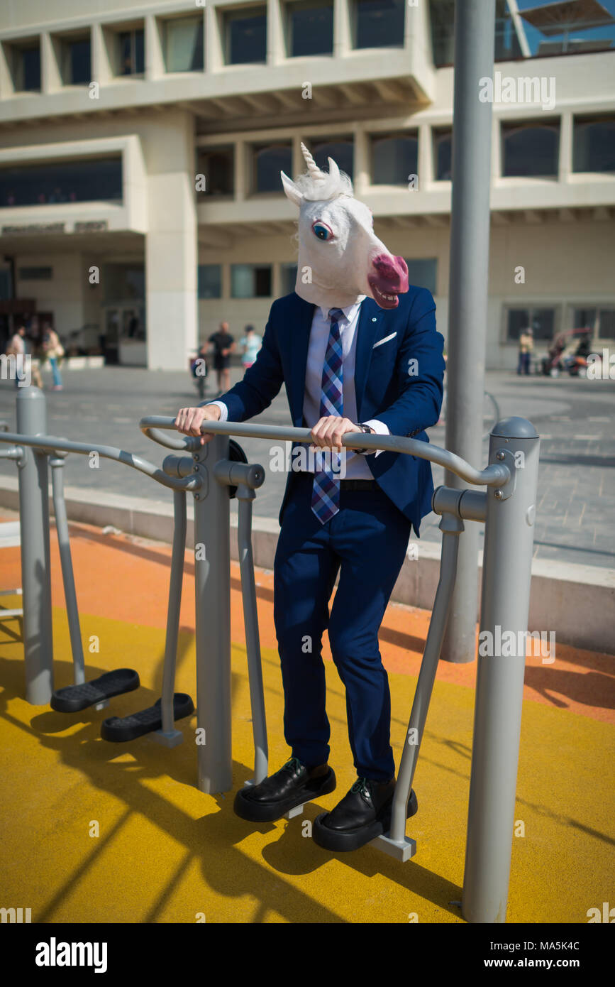 Funny man in elegant suit and freaky mask does sport near city promenade. Stock Photo