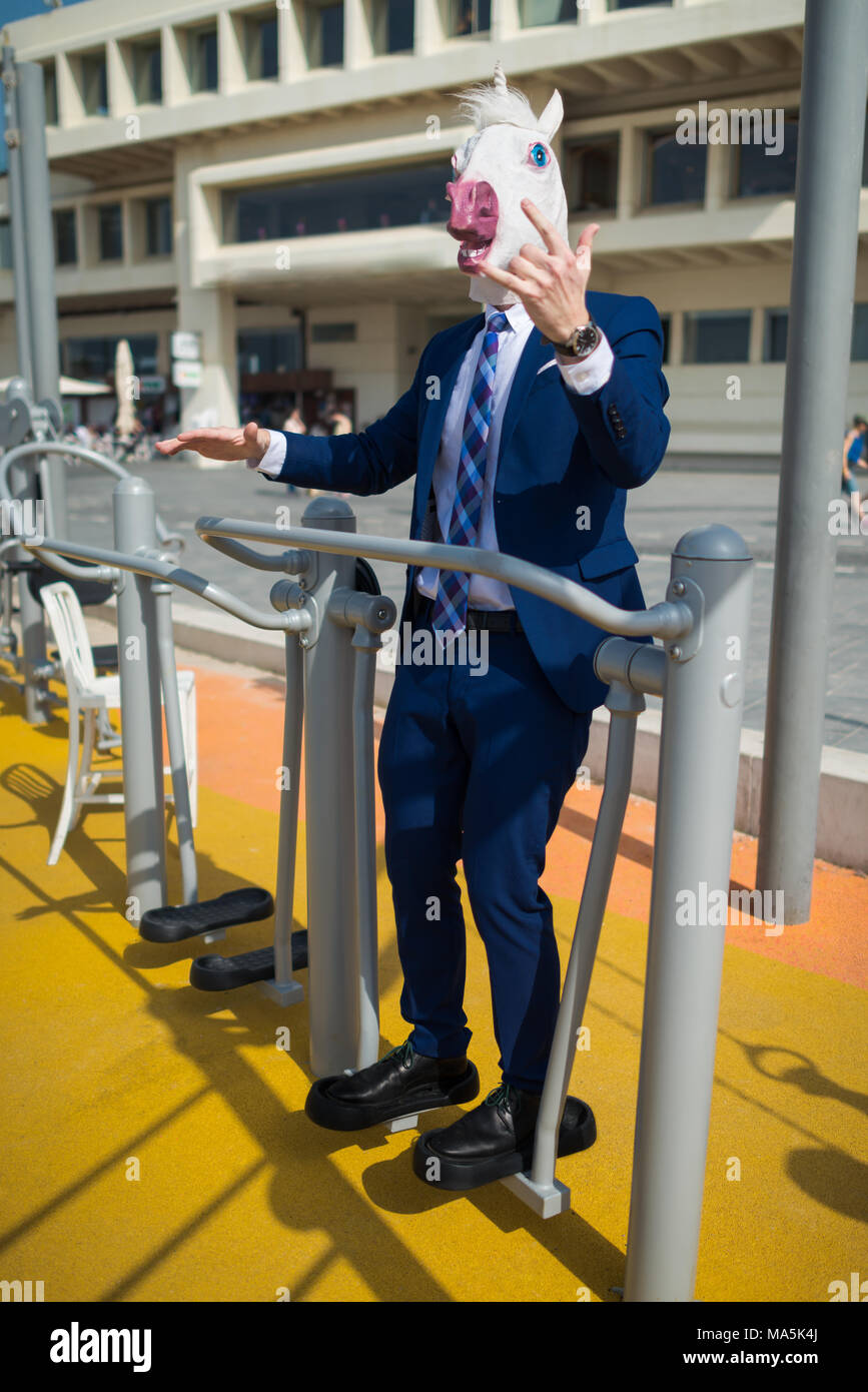 Funny man in mask. Freaky guy in suit pumps muscles and shows strength. Unusual businessman is engaged in fitness at sports ground outdoors Stock Photo