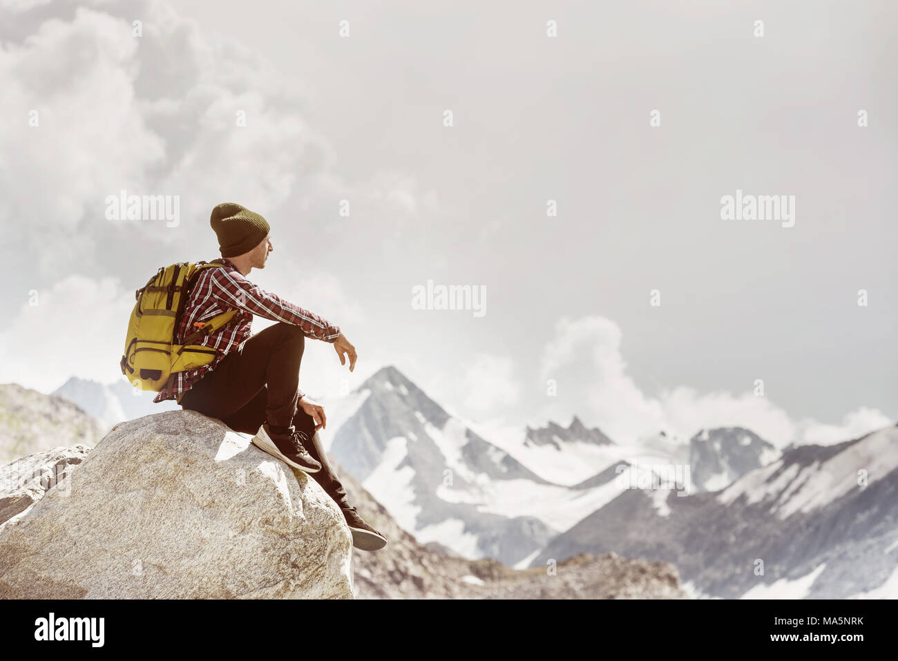 Man backpacker traveller sits rock against mountains Stock Photo