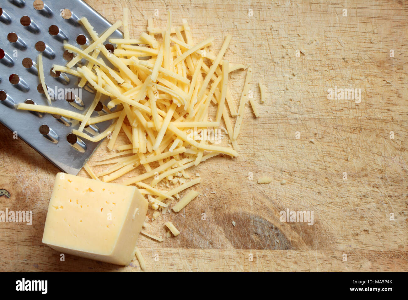 Closeup of grated cheese and grater lying on wooden cutting board Stock Photo