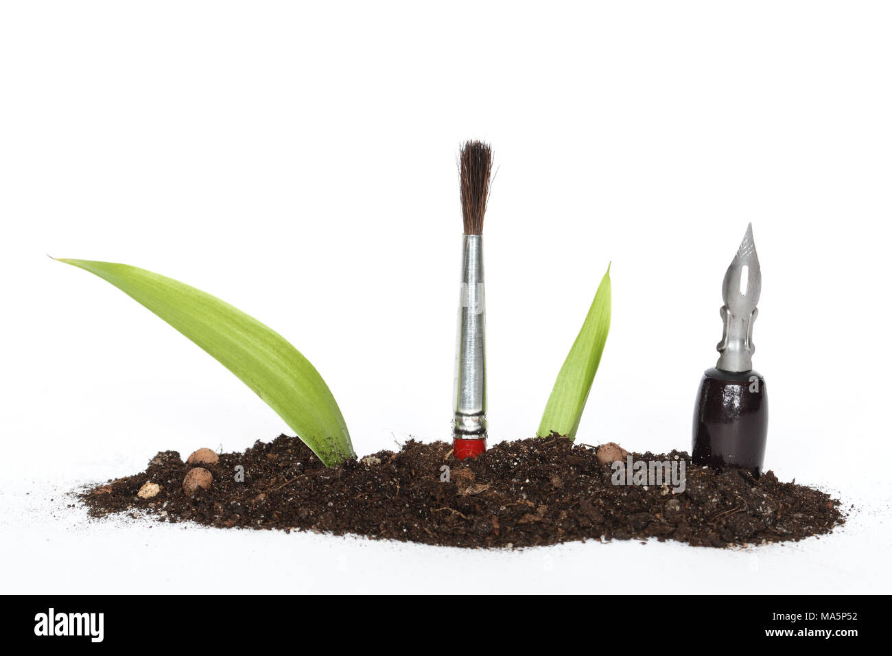 Green leaves, pen and paintbrush inside growing out of earth on white background Stock Photo