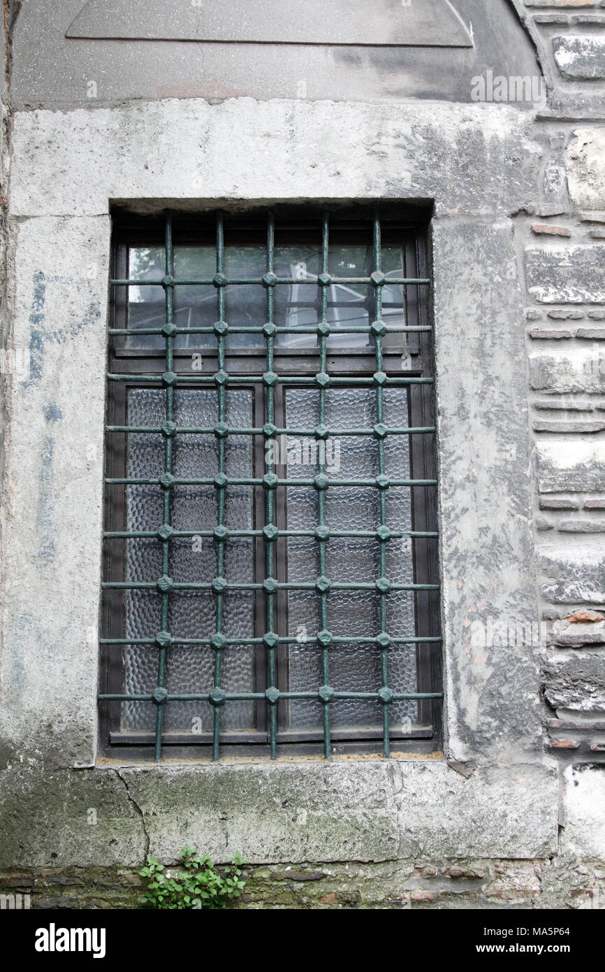 Ancient curch window with metal grating on background with gray stone wall Stock Photo