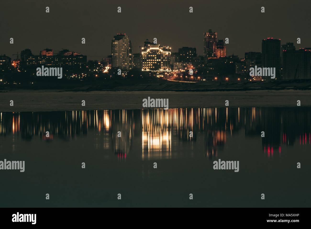 Night city view with lots of lights and its reflection in a river water ...