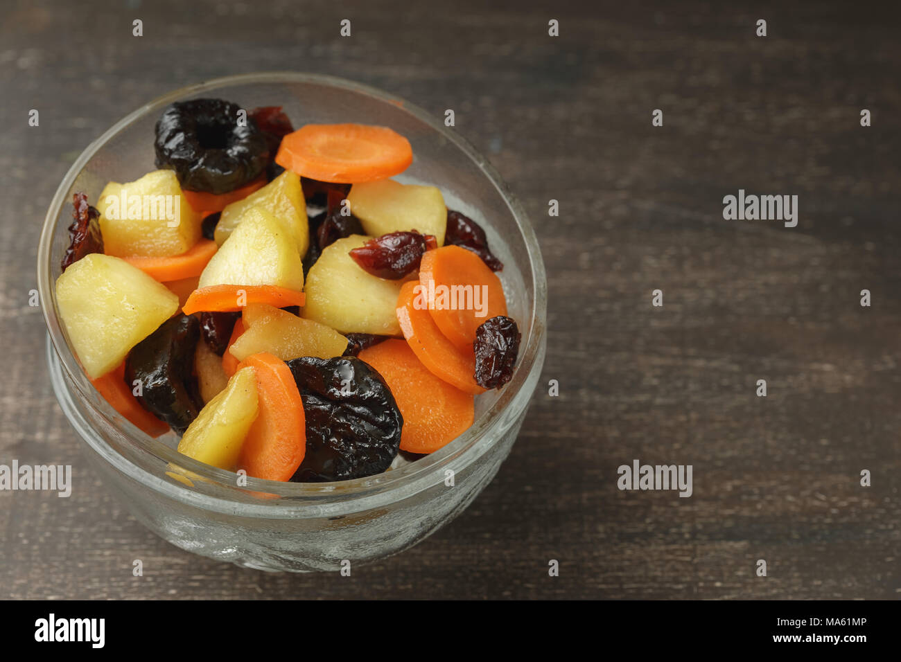 Tzimmes or tsimmes in a vintage glass bowl on the dark wooden table. A ...
