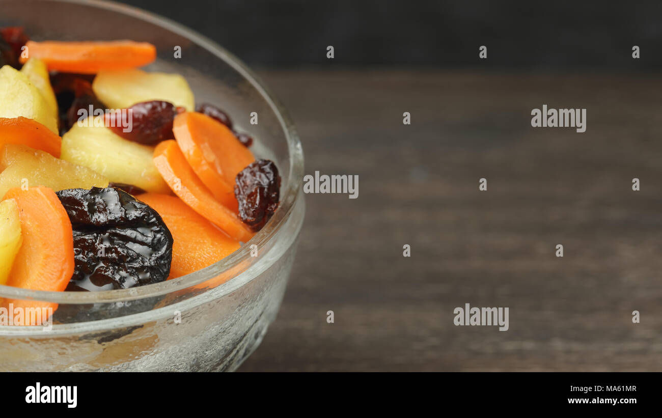 Tzimmes or tsimmes in a vintage glass bowl on the dark wooden table. A ...