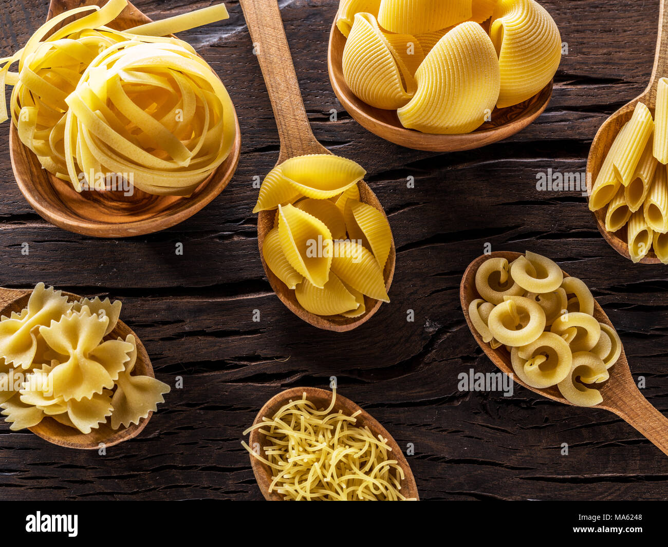 Different pasta types in wooden spoons on the table. Top view. Stock Photo