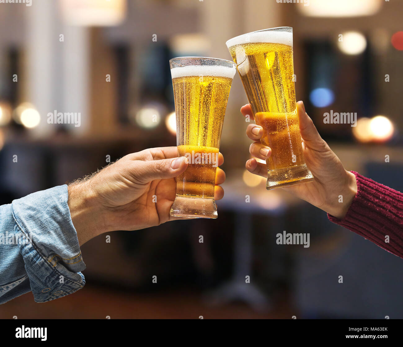 Beer glasses raised in a toast. Close-up hands with glasses. Blurred bar interior at the background. Stock Photo