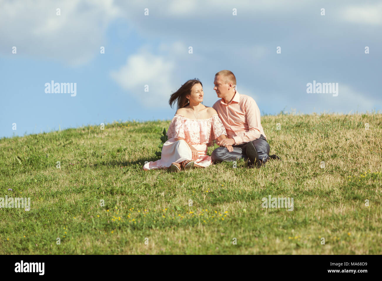 Young man and woman are sitting on the grass on a hill. Stock Photo