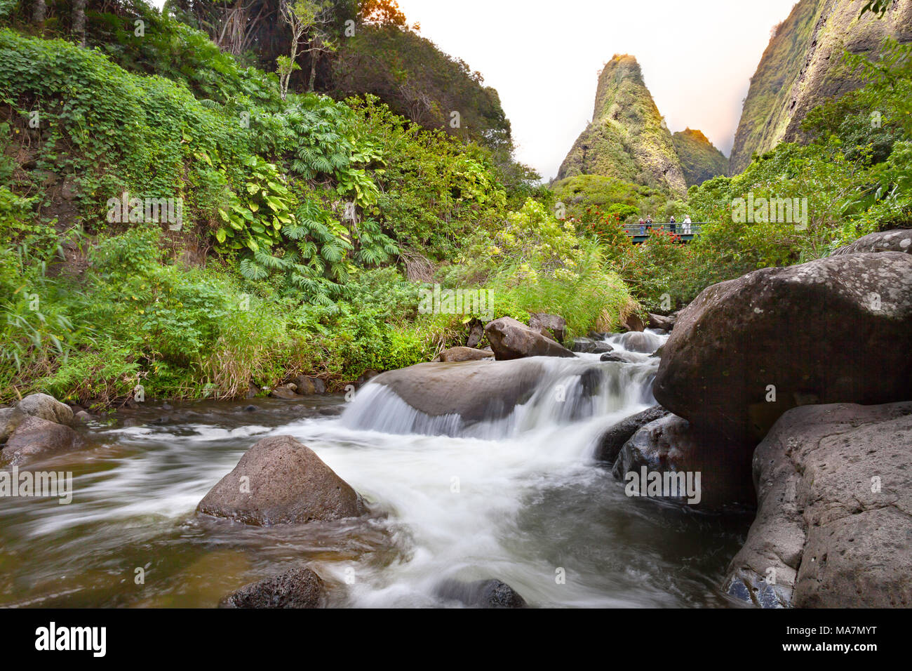 Tourists crossing bridge under the Maui Iao Needle with Iao Stream in the foreground at Iao Valley State Park, Maui, Hawaii. Stock Photo