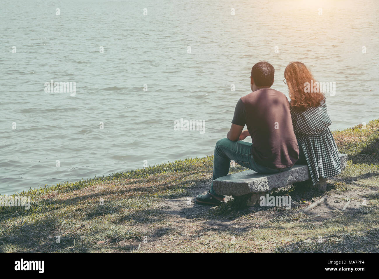 Young couple sitting near lake in the park Stock Photo - Alamy