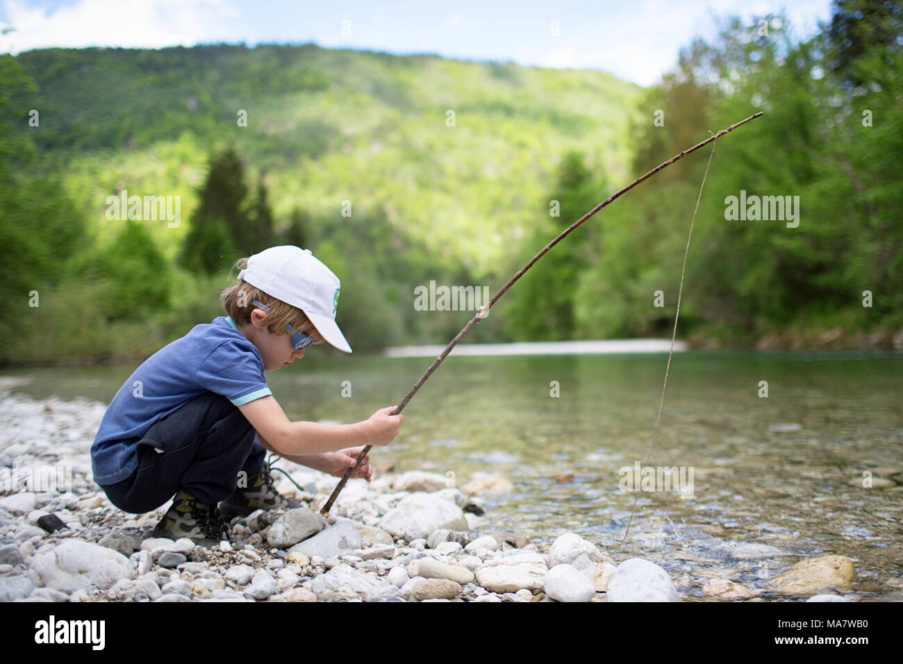 Young blonde boy fishing with a handmade wooden fishing pole on the crystal  clear river, Bohinj, Slovenia Stock Photo - Alamy