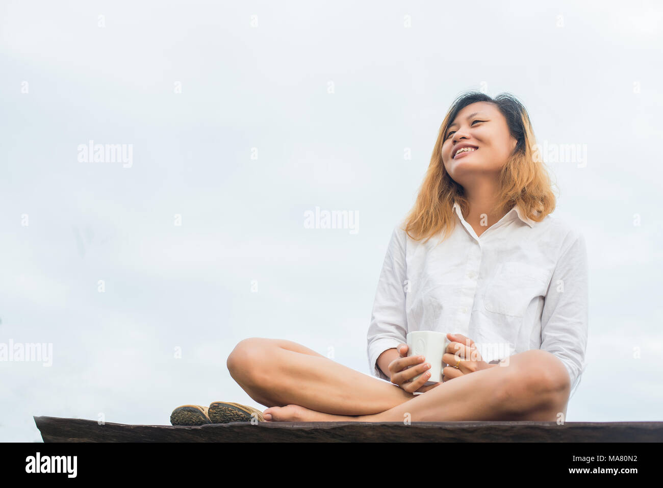 Beautiful woman holding a cup of coffee sitting on bench in the morning ...